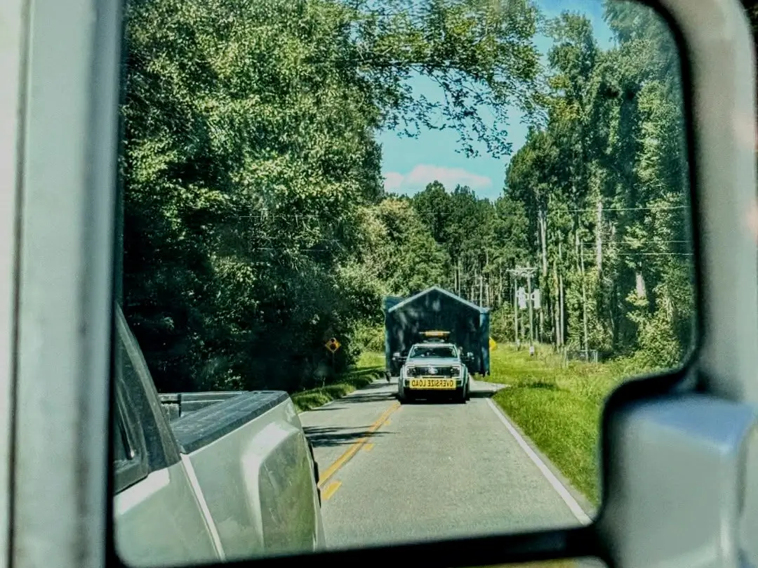 Silverwood building being transported along a tree-lined road, seen in a truck mirror